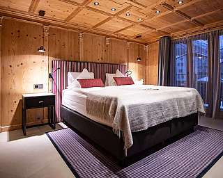 Chambre habillée de bois avec lit double, table de chevet et grandes fenêtres.