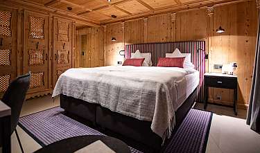 Chambre aux murs revêtus de bois avec lit double, tables de chevet et lumière chaleureuse.
