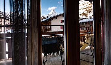 Vue à travers des rideaux sur un balcon avec un paysage enneigé et le Matterhorn.