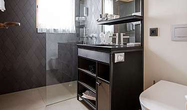 Salle de bains moderne avec douche en verre, meuble vasque noir et fenêtre lumineuse.