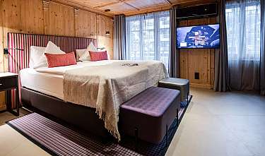 Chambre d'hôtel moderne avec lit double, murs en bois, télévision et grandes fenêtres.