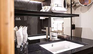 Meuble-vasque de salle de bains moderne avec plan de travail noir, double robinetterie, serviettes et miroirs.