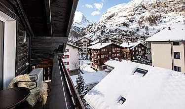Vue depuis le balcon sur des maisons et des montagnes enneigées dans un village alpin.