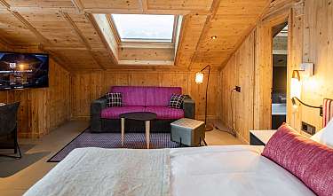 Chambre d’hôtel habillée de bois avec lit, canapé, télévision, bureau et puits de lumière.