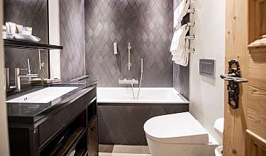 Salle de bain moderne avec des carreaux gris, une baignoire, un lavabo et des serviettes.