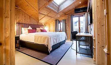Chambre revêtue de bois avec grand lit, bureau et fenêtres.