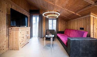 Salon habillé de bois avec un canapé rose, une télévision, une table et un éclairage moderne au plafond.