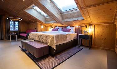 Chambre confortable avec des murs en bois, un lit double, des fenêtres de toit et un coin salon.