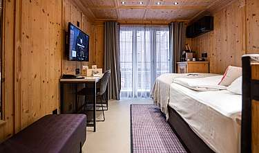 Chambre habillée de bois avec lit, bureau, télévision et fenêtre de balcon.