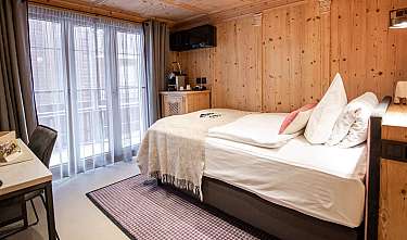 Une chambre d’hôtel lumineuse avec des murs en bois, un grand lit et des portes-fenêtres donnant sur le balcon.