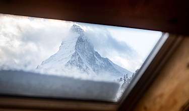 Une montagne enneigée est visible à travers une fenêtre inclinée.