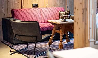 Coin salon confortable avec banquette rose, fauteuil noir et table en bois dans une pièce en bois.