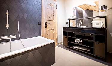 Salle de bains moderne avec baignoire, revêtement mural sombre et détails en bois.