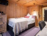 Chambre revêtue de bois avec lit simple, armoire, machine à café et accès ouvert à la salle de bains.