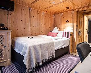 Chambre à revêtement bois avec lit simple, commode et espace salle de bains ouvert.