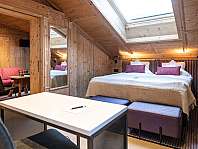 Chambre lambrissée en bois avec lit double, coin salon, table et fenêtre de toit.