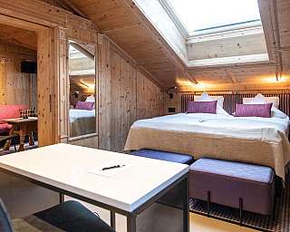 Chambre habillée de bois avec lit double, coin salon et fenêtre de toit.