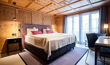 Chambre moderne avec lit double, lambris en bois, baie vitrée et coin salon.