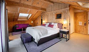 Chambre moderne avec murs en bois, lit double, canapé et fenêtre de toit.
