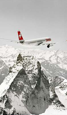 Un avion de passagers survole les Alpes enneigées avec un sommet de montagne caractéristique.