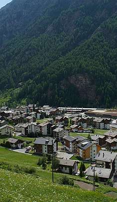Village de montagne avec des maisons dans un paysage de vallée verdoyant devant des pentes boisées abruptes.