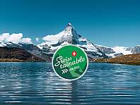 Montagne enneigée au-dessus d’un lac avec le logo Swiss-tainable vert au premier plan.