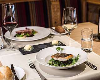 Eleganter Restauranttisch mit Fischgericht, Weingläsern, Brot und Weinflasche.