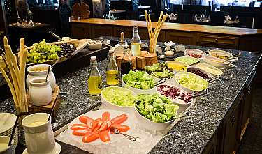 Un buffet de salades riche en légumes, raisins, huiles et gressins sur un comptoir.