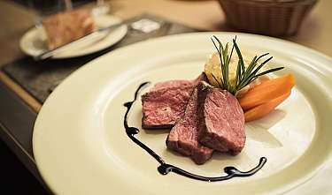 Un steak finement dressé avec des légumes et une branche d'herbes sur une assiette blanche.