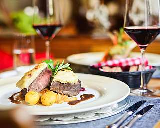 Plat de viande dressé sur une assiette blanche avec garnitures et verre de vin rouge.