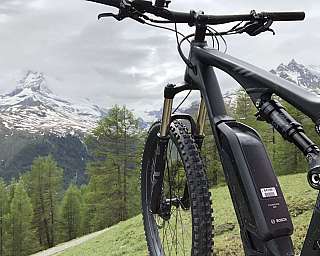 Vélo de montagne noir avec un grand pneu avant devant des montagnes enneigées et une forêt.