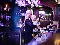Female bartender preparing drinks at a lit bar.