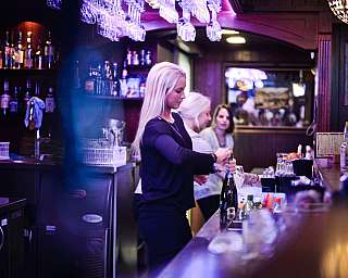 Une barmaid ouvre une bouteille au comptoir dans un bar éclairé.