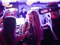 Mehrere Frauen unterhalten sich in einer beleuchteten Bar mit Getränken in der Hand.