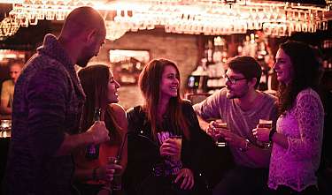 Group of young adults chatting over drinks in a bar with warm lighting.