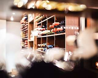 Holzregal mit mehreren Weinflaschen in einem Innenraum, unscharf aufgenommen.