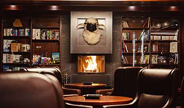 Elegante Lounge mit brennendem Kamin, Bücherregalen und Ledersesseln.