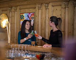 Zwei Frauen stoßen in einer Holzbar mit Weingläsern an.