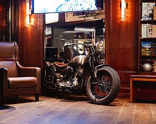 Motorrad steht in einer warm beleuchteten Lounge mit Ledersessel und Bücherregal.