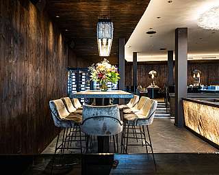 Modernes Restaurant mit Holzwänden, zentralem Tisch, gepolsterten Stühlen und Blumenarrangement.