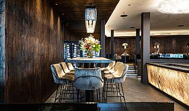Modernes Restaurant mit Holzwänden, zentralem Tisch, gepolsterten Stühlen und Blumenarrangement.