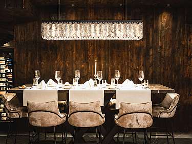 Table dressée avec élégance, avec cave à vins, bougie et chaises rembourrées modernes dans une pièce sombre.