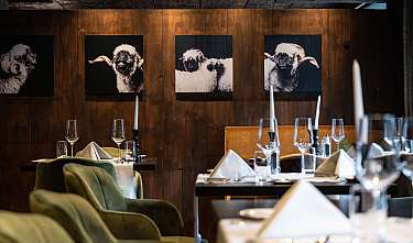 Stilvoll gedeckter Restaurantbereich mit Holzvertäfelung, grünen Stühlen und Ziegenporträts an der Wand.