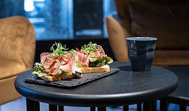 Zwei belegte Brotscheiben auf schwarzem Tablett neben einer blauen Tasse.