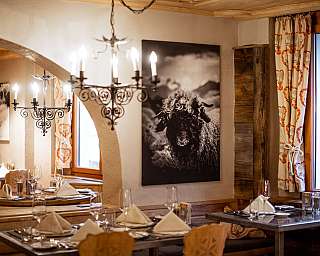 Gemütliches Restaurant mit gedeckten Tischen, Kronleuchtern und Schwarzweiß-Bildern an den Wänden.
