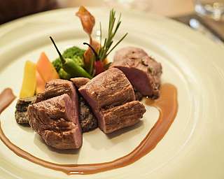 Angerichtetes Fleisch mit Gemüse und Sauce auf einem weißen Teller.
