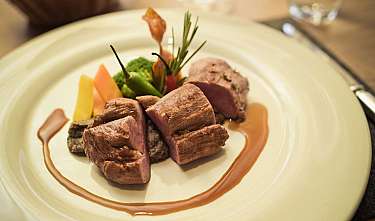 Mehrere Stücke angebratenes Fleisch mit Gemüse und Sauce auf einem weißen Teller