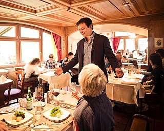 Mann spricht in einem gemütlichen Restaurant mit mehreren Gästen an gedeckten Tischen.