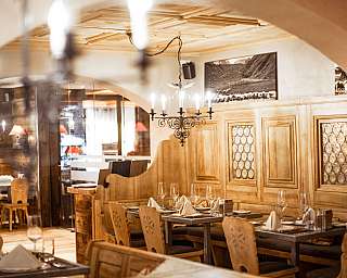 Warmes Restaurant mit gedeckten Tischen, Holzvertäfelung und Kronleuchtern.