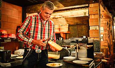 Mann im karierten Hemd serviert Essen an einem Buffet im warm beleuchteten Restaurant.